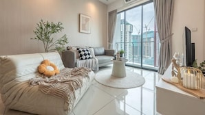 A modern living room with a sofa, armchair, coffee table, and a large window with a view of buildings. - Bliss Residence Old Klang Road by FEEL HOME (Kuala Lumpur)