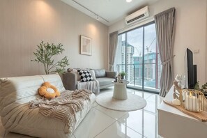 En moderne stue med sofa, lænestol, sofabord og et stort vindue med udsigt til bygninger.
