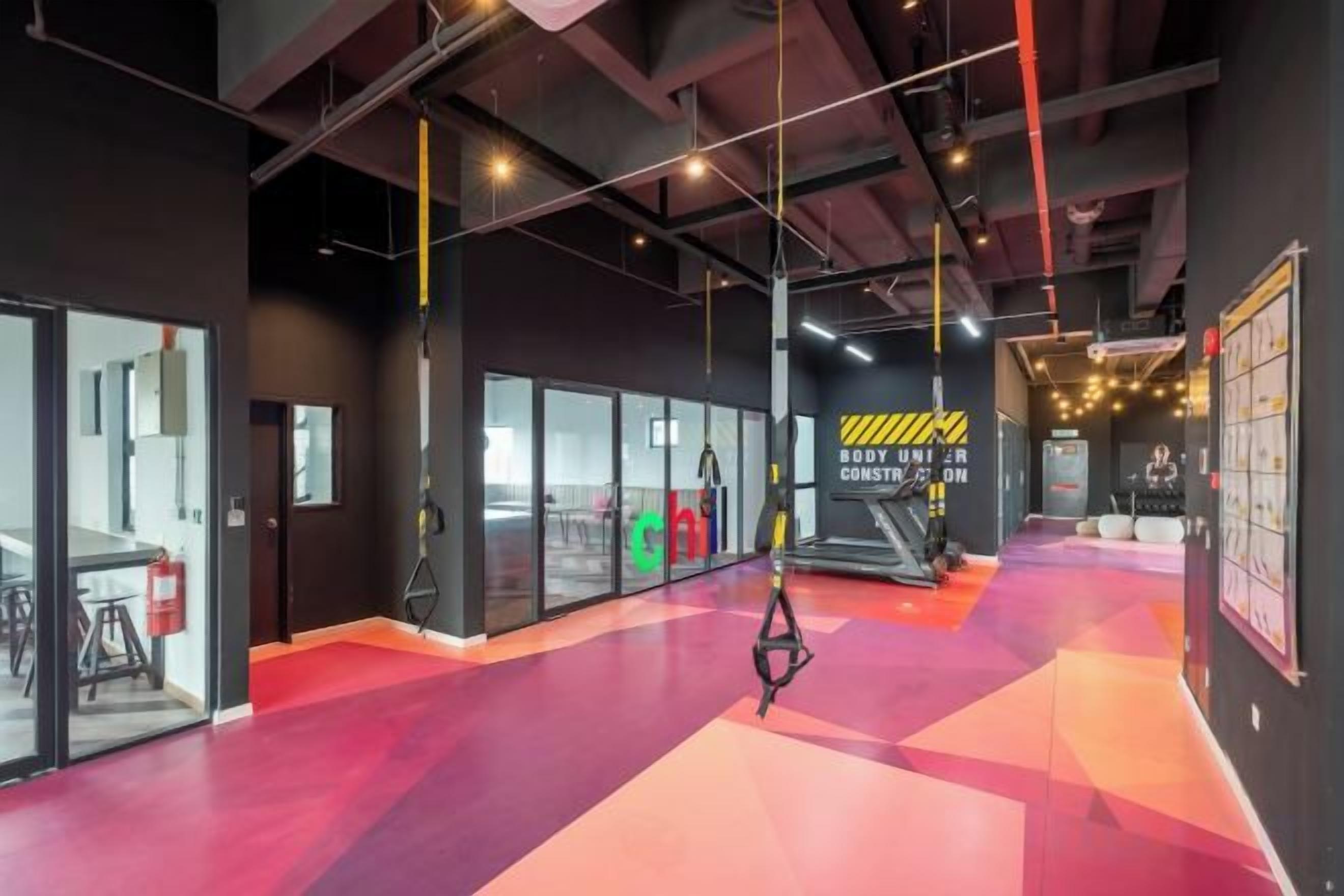 Academia com equipamentos de ginástica, piso vermelho e parede preta com uma placa amarela.