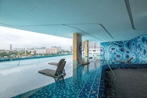 En indendørs swimmingpool med udsigt over byen, liggestole og en væg med mønster.