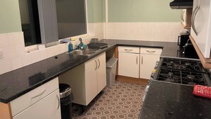 Een compacte keuken met een zwart aanrecht, witte kastjes, een roestvrijstalen spoelbak en een gasfornuis.
