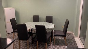 Een eethoek met een ronde tafel, zes stoelen, een koelkast en een vloer met een patroon.