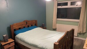 Een eenpersoonskamer met een houten hoofdbord, een nachtkastje, een lamp en een raam met gordijnen.