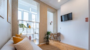 A modern living room with a sofa, a TV mounted on the wall, and a large window. - Nomad s Easy Stay - Duque Studio XIX (Porto)