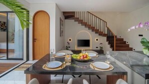 A modern dining area with a marble table, white chairs, and a fruit bowl centerpiece. - Nidya Villa Canggu (Bali)