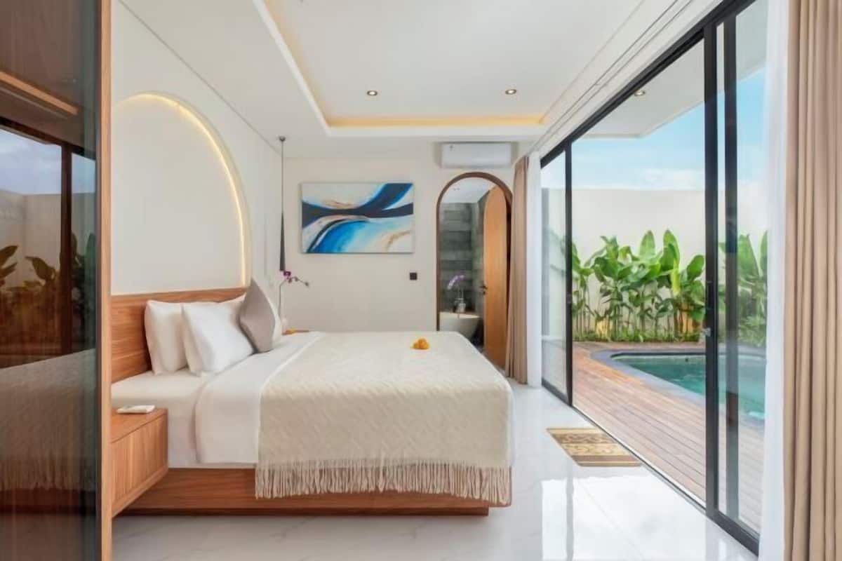 A modern bedroom with a large bed, a view of a swimming pool, and a glass door leading to a balcony.