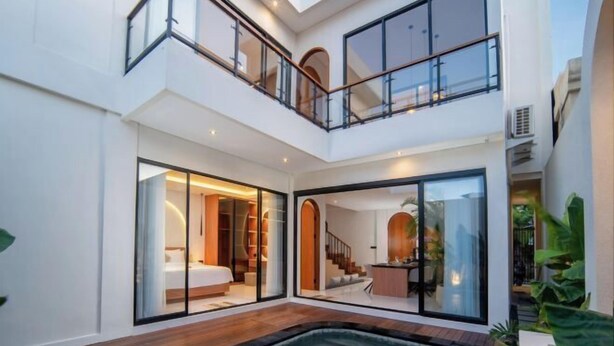 A modern, multi-level residential interior with a central swimming pool, glass doors leading to bedrooms, and a staircase connecting the levels. - Nidya Villa Canggu (Bali)
