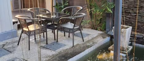 Un patio con mesa y sillas, rodeado de plantas y una pequeña fuente.