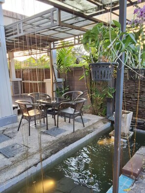 A patio area with a table and chairs, surrounded by plants and a small water feature. - Spacious Entire House With Shared Fitness Room and Shared Indoor Pool in Club (Pathum Thani)