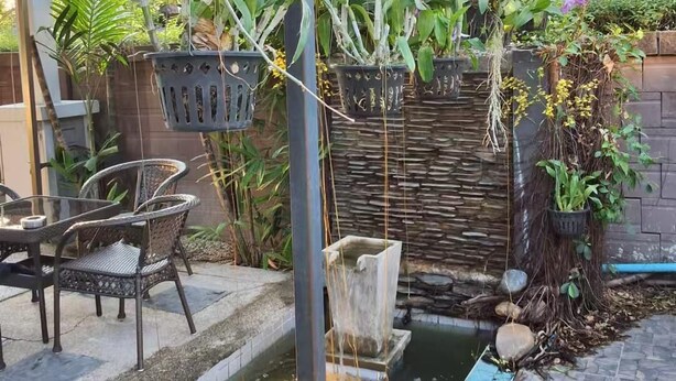 Un jardín con un pequeño estanque, plantas en macetas y mobiliario de exterior.