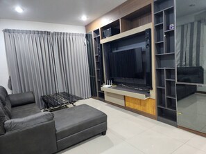 A living room with a sofa, a coffee table, a TV, and built-in shelving. - Spacious Entire House With Shared Fitness Room and Shared Indoor Pool in Club (Pathum Thani)