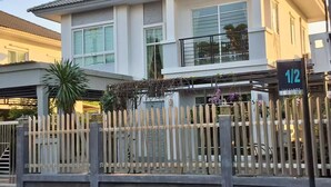 Un edificio residencial de dos plantas con balcón, entrada protegida por un portón y un cartel con el número de la propiedad.