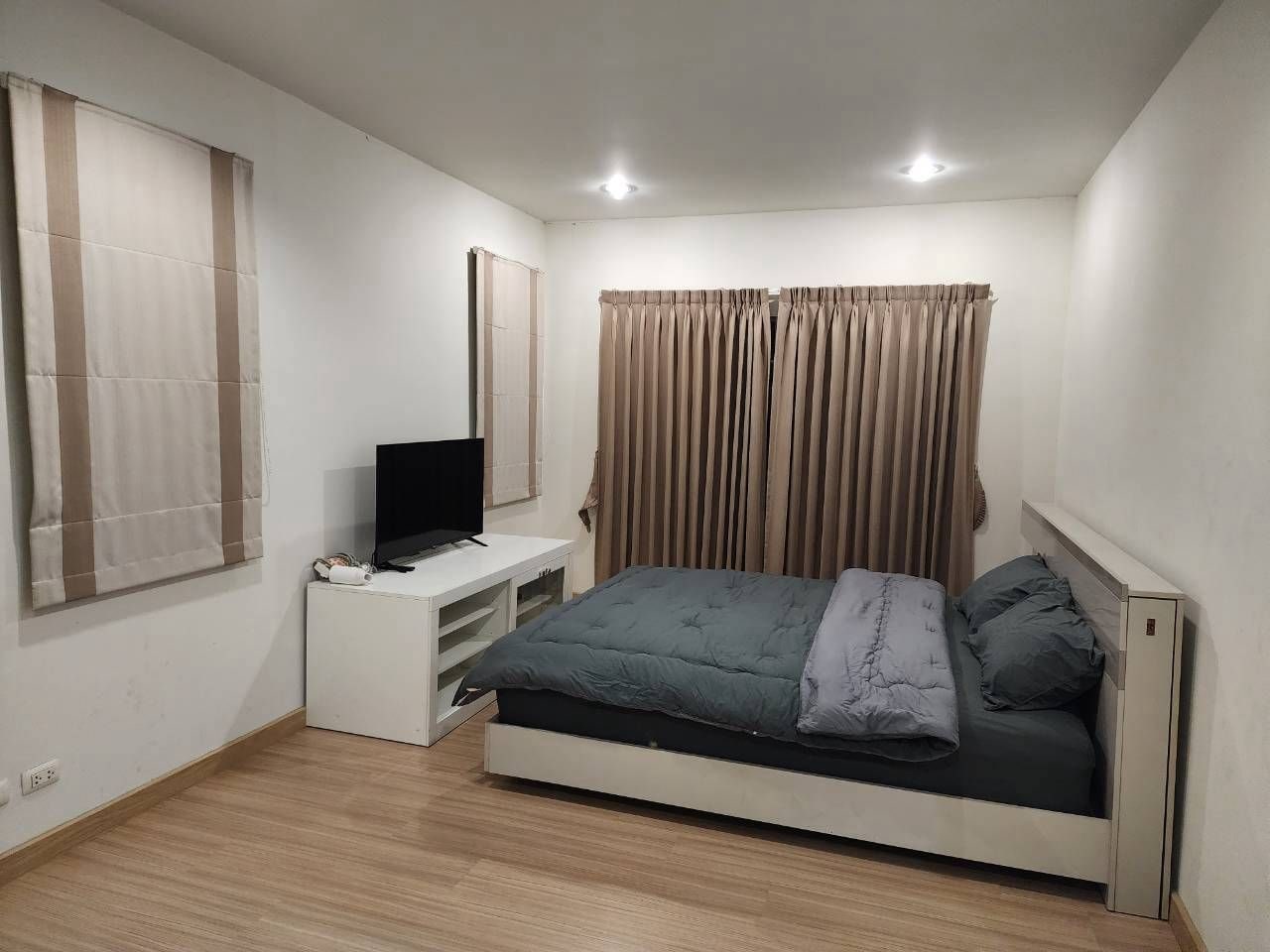 A bedroom with a bed, a TV on a stand, and curtains on the windows.
