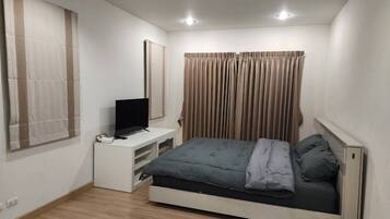 A bedroom with a bed, a TV on a stand, and curtains on the windows.