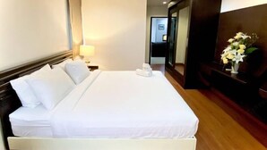 A neatly made bed with white linens, a bedside lamp, and a vase with flowers on a wooden nightstand. - 14Place Sukhumvit Villa @ Terminal 21 Bangkok (Bangkok)