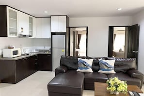 A modern living room with a dark brown leather sofa, two decorative pillows, a coffee table with a floral arrangement, and a kitchen area with white cabinets and appliances. - 14Place Sukhumvit Villa @ Terminal 21 Bangkok (Bangkok)