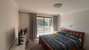 Un dormitorio con cama, escritorio, silla, ventana con cortinas y vista al exterior.