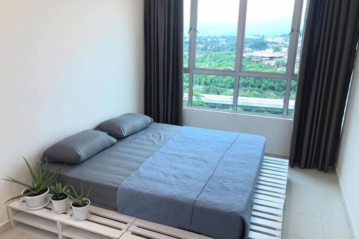 Um quarto com uma cama, uma janela com vista e três plantas em vasos sobre uma mesa de cabeceira.