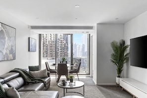 A modern living room with a sofa, coffee table, TV, and balcony with city views. - A Modern 2BR Apt with City Views, FREE Parking (Southbank)
