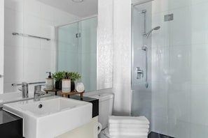 A modern bathroom with a large sink, mirror, shower, and a towel rack.