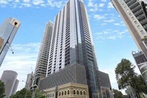 Un edificio alto y moderno con una fachada única, rodeado de otras construcciones de gran altura.