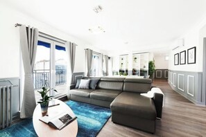 A modern living room with a sectional sofa, a coffee table, and a view of the outdoors. - Horizon House (Paris)