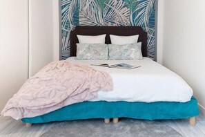 A bed with a white and teal bedspread, a pink blanket, and a book on the bed. - Horizon House (Paris)