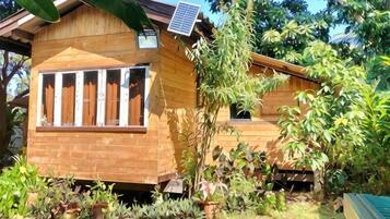 Una casa de madera con un panel solar, rodeada de vegetación exuberante.