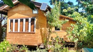 A wooden house with a solar panel, surrounded by lush greenery. - Num Homestay (Mae Tha)
