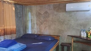 A single bed with a blue mattress, a wooden headboard, a small bedside table, and an air conditioning unit on the wall. - Num Homestay (Mae Tha)