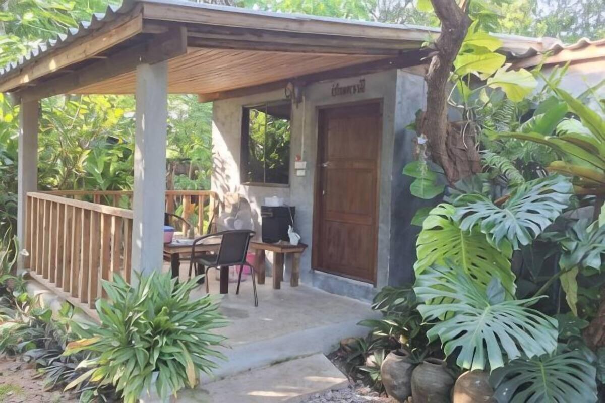 A covered outdoor area with a table and chairs, a door, and lush greenery.