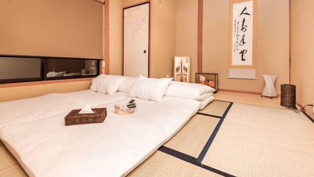 A traditional Japanese-style room with tatami flooring, a large bed, a sliding door, and a wall-mounted artwork. - KIRAKU・ENRINON (Kyoto)