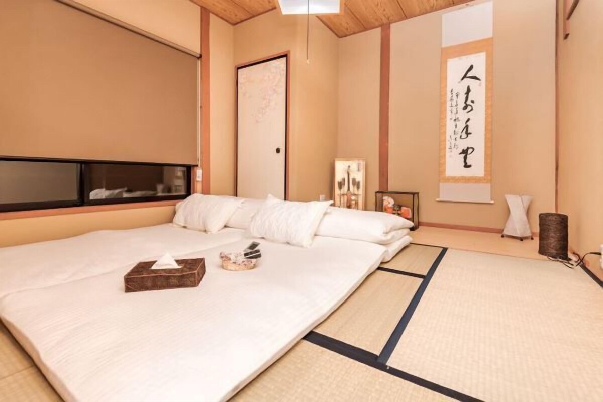 A traditional Japanese-style room with tatami flooring, a large bed, a sliding door, and a wall-mounted artwork.