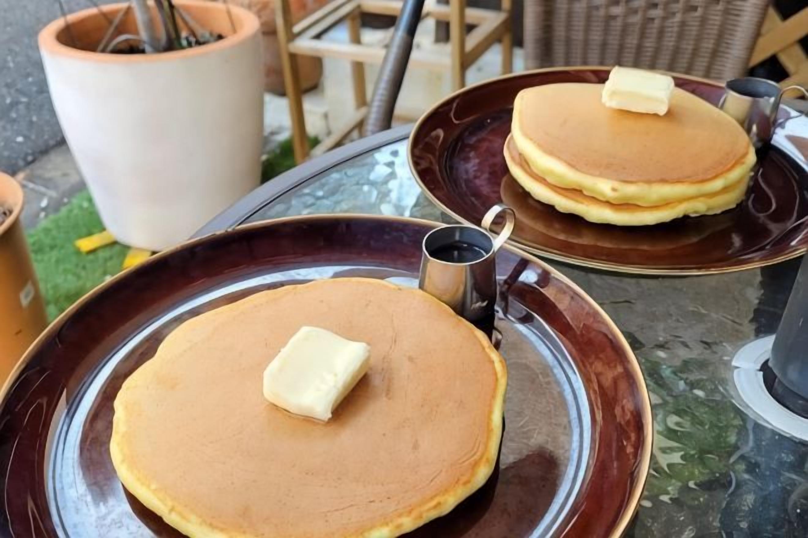 Two plates of pancakes with butter on a table.