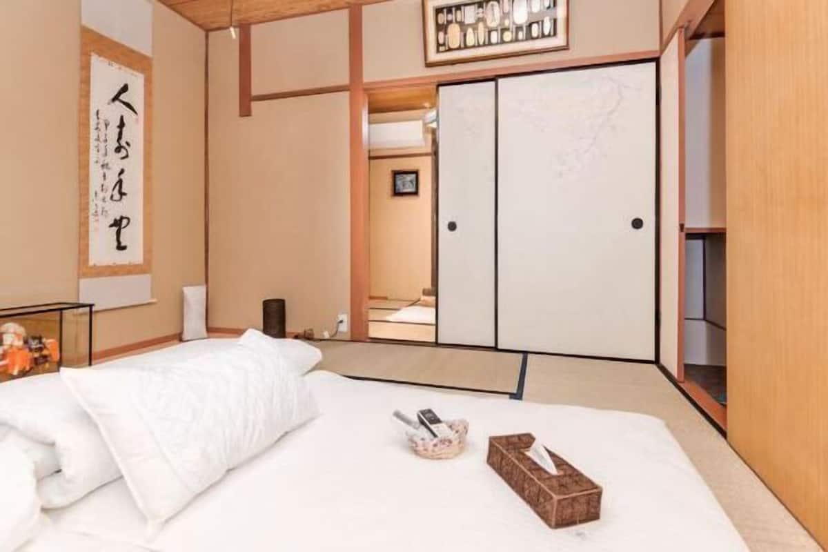 A traditional Japanese-style room with tatami flooring, a bed with white bedding, a wooden wardrobe, and a shoji screen door.