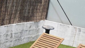 Duas poltronas de madeira com almofadas, uma mesa pequena e diversas plantas verdes num jardim.