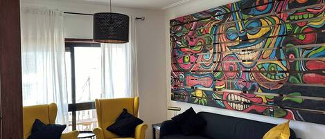 A living room with a sofa, two armchairs, a patterned rug, and a colorful abstract painting on the wall.