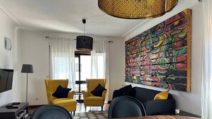 Uma sala de estar moderna com uma mesa de jantar de madeira, poltronas amarelas, um sofá preto e uma pintura abstrata colorida na parede.