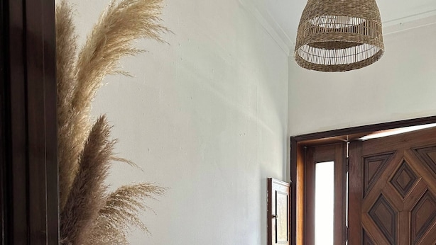 Um corredor com porta de madeira, um aparador branco com planta e luminária de vime suspensa.