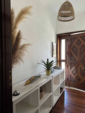 A hallway with a wooden door, a white console table with a plant, and a hanging wicker light fixture. - 5 Room House, Next to Golf Course Quinta do Fojo (Vila Nova de Gaia)