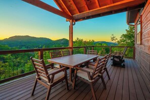 A wooden deck with a table and chairs, overlooking a mountainous landscape. - 🌅 Sunset Ridge ⛰️ Sunset Mountain Views, Fire Pit, Hot Tub & Game Room (Sevierville)