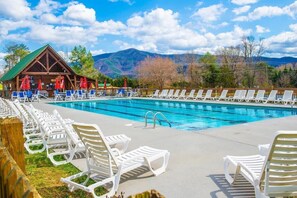 A swimming pool with lounge chairs and a wooden building with a green roof. - 🌅 Sunset Ridge ⛰️ Sunset Mountain Views, Fire Pit, Hot Tub & Game Room (Sevierville)