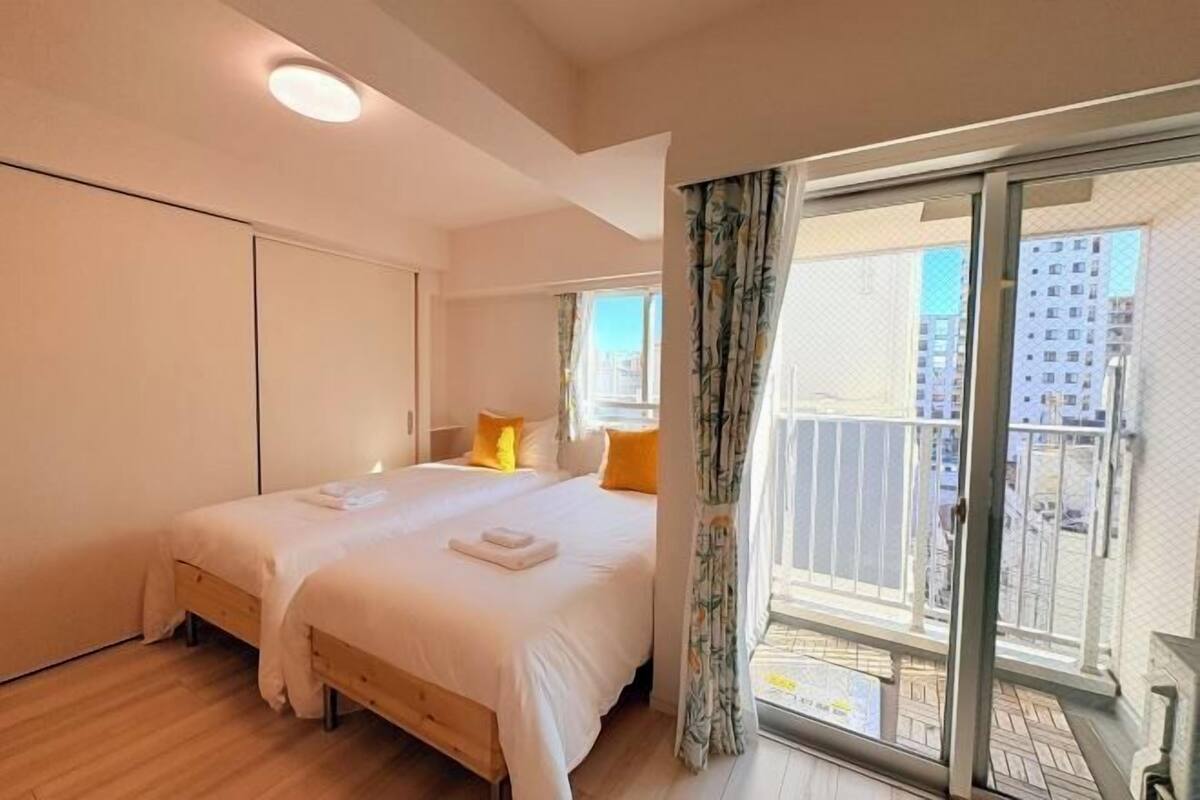 A bedroom with a large bed, a sliding glass door to a balcony, and a view of buildings.
