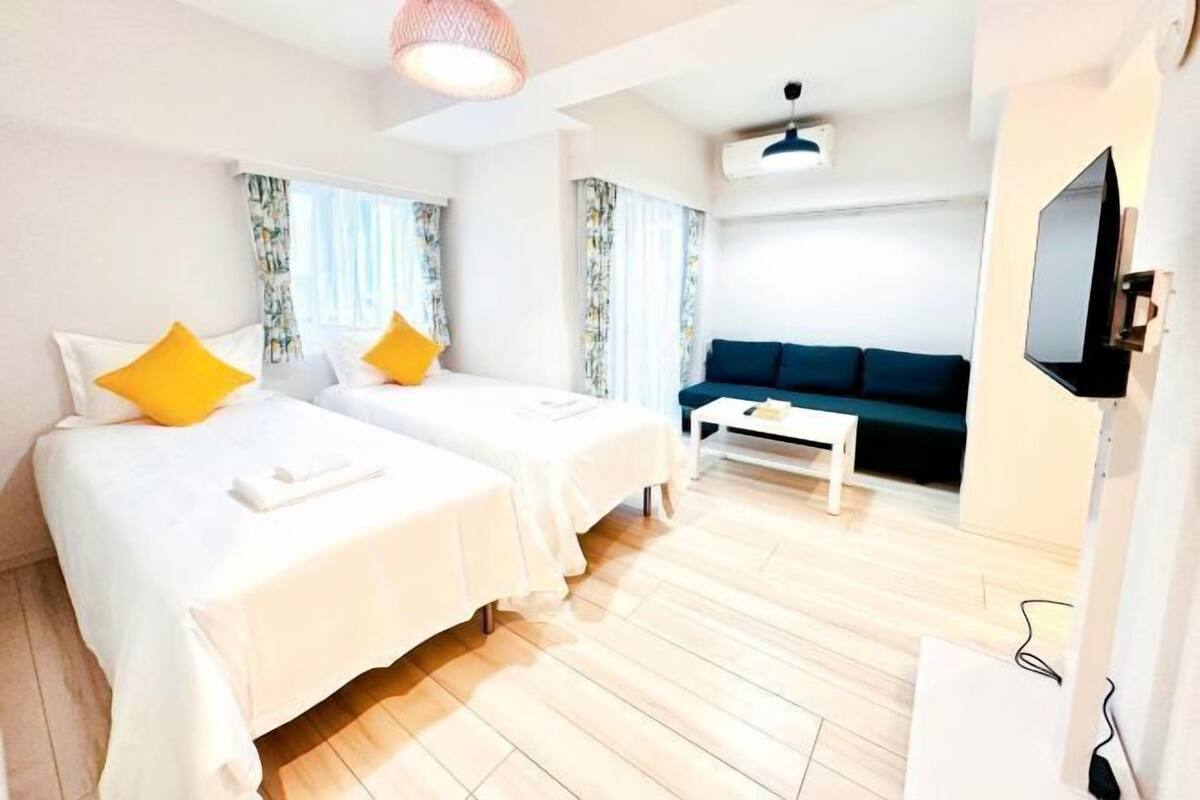 A hotel room with two beds, a sofa, a coffee table, a TV, and a ceiling fan.