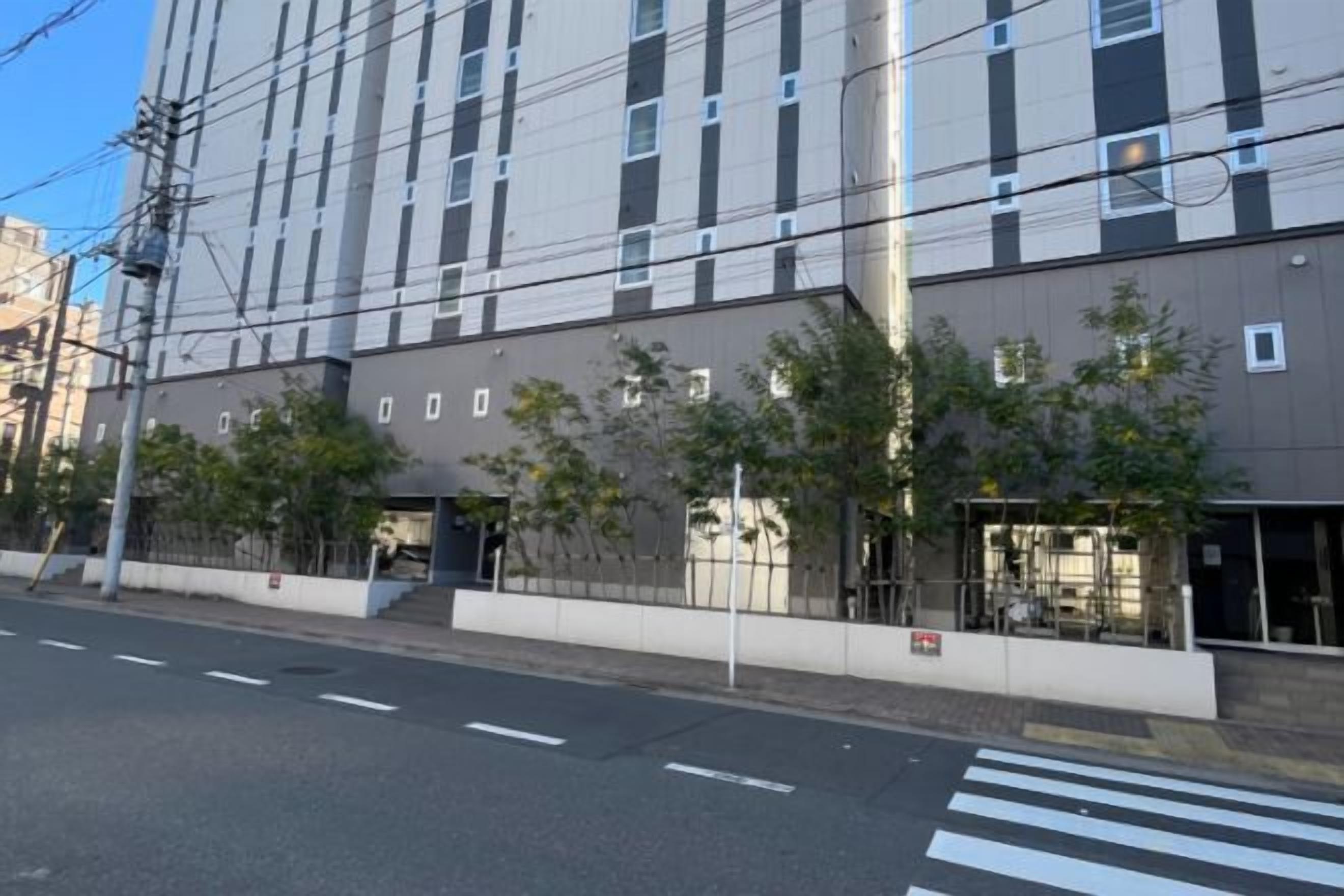 Un edificio de varios pisos con fachada plana, un paso de peatones y una calle sin vehículos a la vista.
