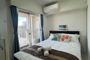 A hotel room with a bed, a window with curtains, an air conditioning unit, and a painting on the wall. - REGNO CONFORT ASAKUSA Ⅳ (Tokyo)