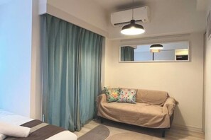 A room with a bed, a sofa, a window with a view, and an air conditioning unit. - REGNO CONFORT ASAKUSA Ⅳ (Tokyo)