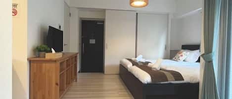 Une chambre à coucher avec un lit, une commode en bois, un téléviseur et un luminaire suspendu.