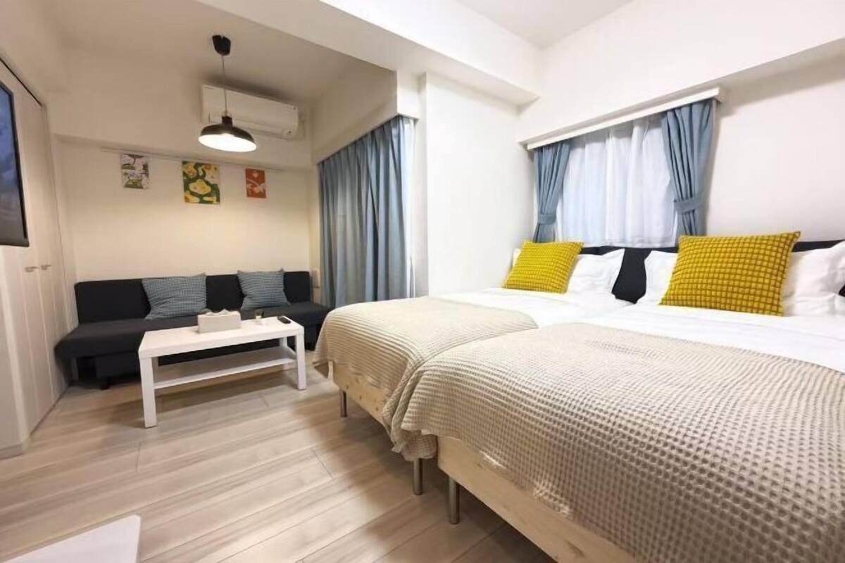 A modern hotel room with a bed, a sofa, a small table, and a window with curtains.