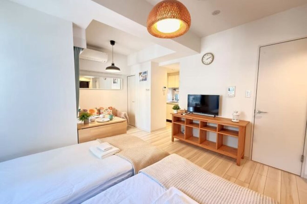 A hotel room with two beds, a TV, a wooden cabinet, a clock, and a door.